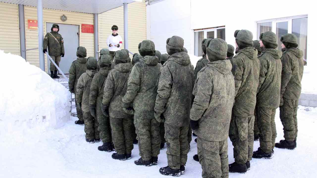 Skupina mužov v zimných vojenských uniformách stojí v rade pred budovou počas mobilizačnej kontroly