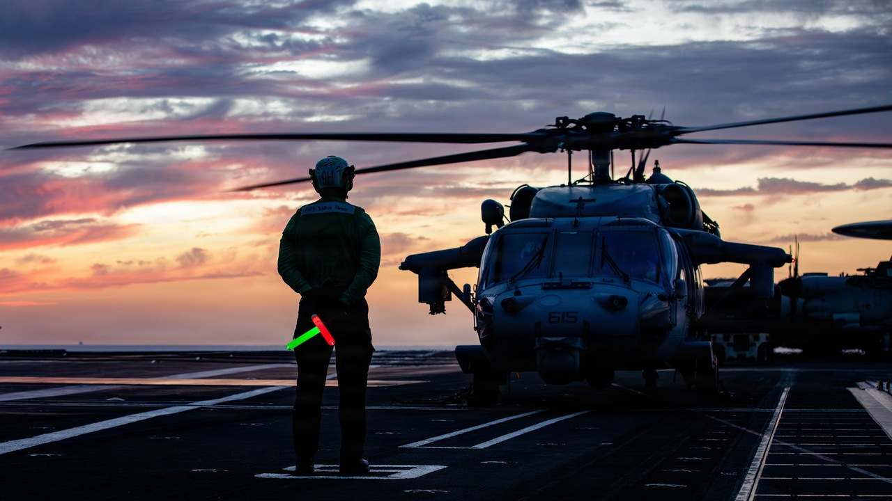 Americký námorník signalizuje vrtuľníku MH-60S Sea Hawk na palube lietadlovej lode USS Gerald R. Ford pri západe slnka