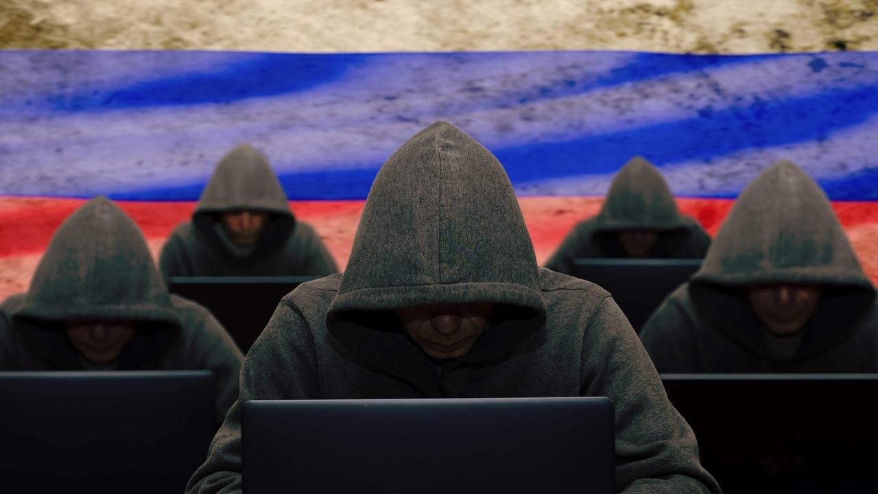 Skupina anonymných osôb pracujúcich na notebookoch pred ruskou vlajkou, ilustračná fotografia kybernetických operácií
